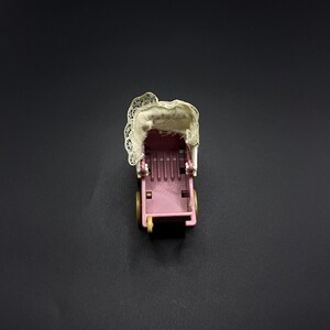 Puede incluir: Un cochecito de juguete rosa en miniatura con una capota de encaje blanco y ruedas amarillas. El cochecito tiene un diseño clásico, con un asiento y un asa. La capota está ligeramente desgastada, lo que añade encanto vintage.