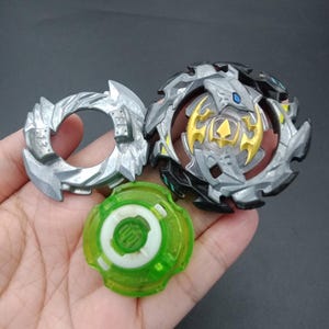 May include: A three-part toy set comprising a silver ring, a black and silver top with gold detailing, and a green and white base. The toys have detailed designs and sharp edges, possibly for a competitive game or as collectables.