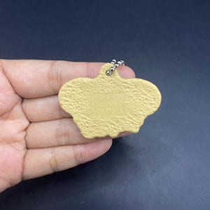 K&ouml;nnte beinhalten: Ein hellbrauner Schl&uuml;sselanh&auml;nger mit strukturierter Oberfl&auml;che und silberner Kugelkette. Der Schl&uuml;sselanh&auml;nger hat eine einzigartige, unregelm&auml;&szlig;ige Form. Der Text "&copy; A.T. B.CHINA 2699513" ist auf der Oberfl&auml;che aufgedruckt.