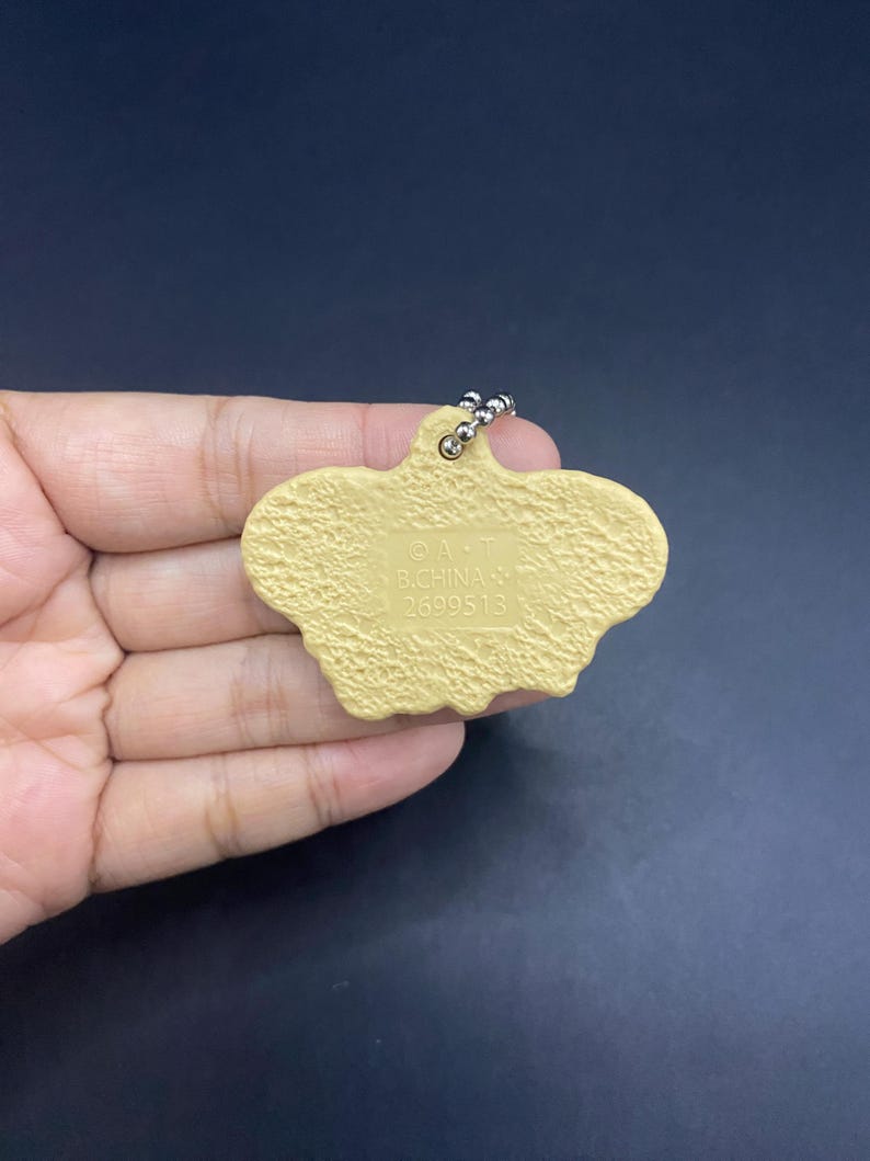 K&ouml;nnte beinhalten: Ein hellbrauner Schl&uuml;sselanh&auml;nger mit strukturierter Oberfl&auml;che und silberner Kugelkette. Der Schl&uuml;sselanh&auml;nger hat eine einzigartige, unregelm&auml;&szlig;ige Form. Der Text "&copy; A.T. B.CHINA 2699513" ist auf der Oberfl&auml;che aufgedruckt.