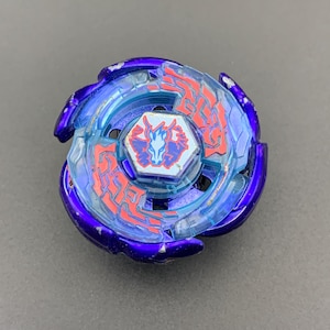 Könnte beinhalten: Ein kreisförmiges Kreiselspielzeug mit einem metallisch violetten Außenring und einem durchscheinenden hellblauen Innenteil. Die Mitte zeigt ein sechseckiges Emblem mit einer weißen Pferdekopf-Grafik auf rot-blauem Grund, akzentuiert durch rote Blitzmuster.
