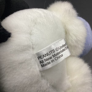 May include: White and blue plush toy with a Peanuts logo tag that reads "PEANUTS &copy;United All New Materials/Syn Made in China".