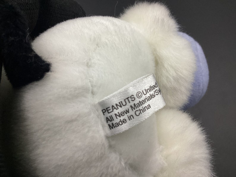 May include: White and blue plush toy with a Peanuts logo tag that reads "PEANUTS &copy;United All New Materials/Syn Made in China".