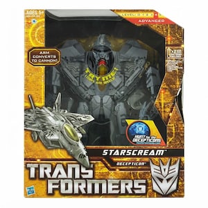 Puede incluir: Una figura de acción de Transformers Starscream en su empaque original. La caja presenta un robot gris, una ilustración de un avión de combate y texto que incluye "Try Me! Lights and Speech", "Arm Converts to Cannon" y "Hunt for the Decepticons".