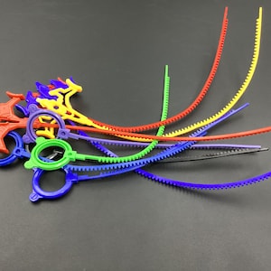 Pode incluir: Um conjunto de amarras de cabo de plástico coloridas com uma borda serrilhada. As amarras são de várias cores, incluindo vermelho, amarelo, azul, verde e preto.