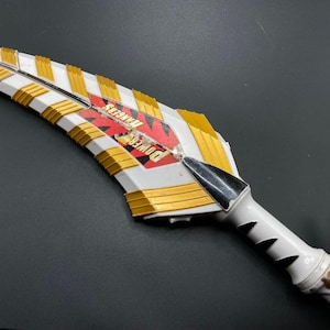 Può includere: Spada giocattolo di plastica bianca e dorata con la scritta "Power Rangers" stampata sul lato.