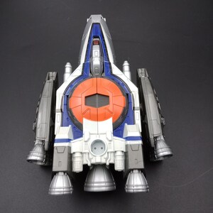 May include: A toy spaceship with a white, blue, orange, and silver color scheme. The toy has multiple engines and wings, and a detailed design. The spaceship is a futuristic toy.