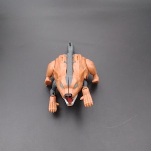 May include: A tan and gray toy robot in the shape of a wolf. The toy has blue eyes, a gray spine, and articulated limbs. The wolf's mouth is open, revealing white teeth. The toy is on a gray surface.