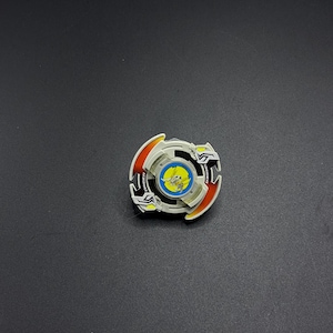 Könnte beinhalten: Ein weißer, roter und gelber Beyblade mit einem blauen und gelben Zentrum. Der Beyblade hat ein schwarz-weißes Design auf der Außenseite und die Wörter "Dragoon" und "Attack" sind darauf gedruckt.