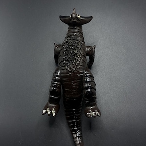 May include: A dark brown plastic toy dinosaur with a spiky back and a long tail. The dinosaur is posed standing on all fours with its head tilted back.