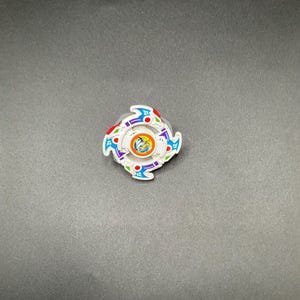 May include: A white spinning top toy with a circular design and multi-coloured accents. The toy features blue, red, green, and purple details. The centre has a circular design with a blue and yellow image.