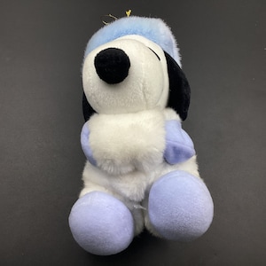 May include: A white plush toy dog wearing a blue hat and mittens. The dog is sitting with its paws tucked in front of it.