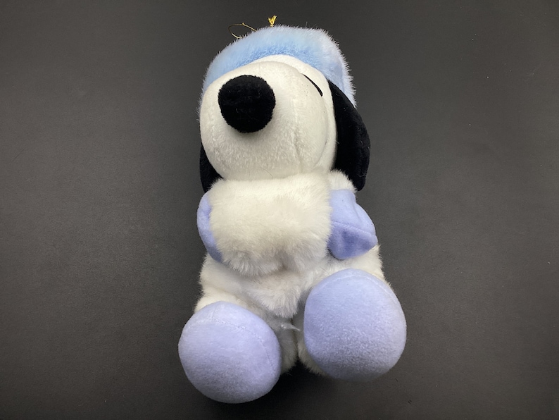 May include: A white plush toy dog wearing a blue hat and mittens. The dog is sitting with its paws tucked in front of it.