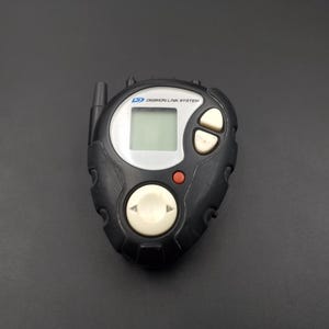 May include: Black and grey Digimon Link System handheld game with a small antenna, a red button, and a white button with a directional arrow. The screen displays "Digimon Link System".