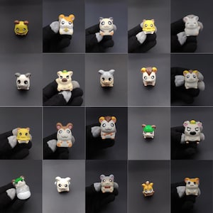 May include: A collection of small, colorful hamster figurines. Each figurine has a unique design, with variations in color and accessories. The hamsters are displayed against a dark background, showcasing their details.