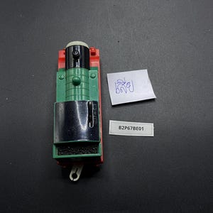 Könnte beinhalten: Eine Spielzeug-Lokomotive in Rot, Grün, Schwarz und Weiß. Der Motor hat einen schwarzen Schornstein und einen grünen Körper. Ein kleines weißes Etikett mit dem Text "B2P67BE01" befindet sich neben dem Zug.