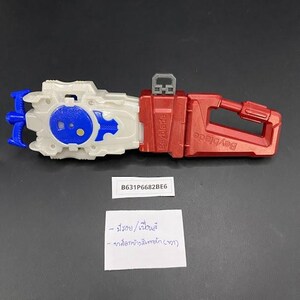 May include: A red and white Beyblade launcher toy with blue and white accents. The launcher has a handle and a trigger. The text "Beyblade" is visible on the side. The toy has the text "B631P6682BE6" on a sticker.