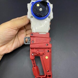 May include: A red, white, and blue plastic toy with a handle. The toy has a circular top with a black center and blue ring. The handle is red and has a gray latch. The toy is made in Vietnam.
