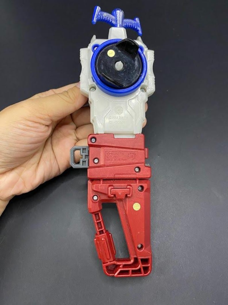 May include: A red, white, and blue plastic toy with a handle. The toy has a circular top with a black center and blue ring. The handle is red and has a gray latch. The toy is made in Vietnam.