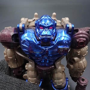 以下が含まれることがあります： メタリックブルーとブラウンのオプティマスプライマルアクションフィギュア。赤い目と胸に「OPTIMUS」の文字が入ったゴリラのようなデザインです。このフィギュアはコレクターズアイテムです。