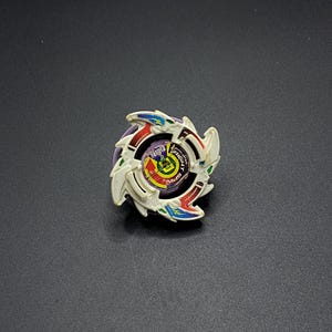 May include: A white, purple, red and blue Beyblade with a dragon design. The Beyblade has a clear plastic centre with a green and yellow design. The Beyblade is on a black background.
