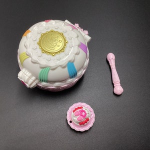 May include: A white and pink plastic toy compact with a gold star design and a matching pink wand and a small pink plate with a pink and white design.