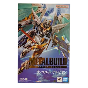 May include: A Metal Build Dragon Scale Lancelot Albion action figure box featuring a white and gold mechanical robot with large translucent green wings, a red sword, and blue accents against a blue sky background with Bandai Namco branding.