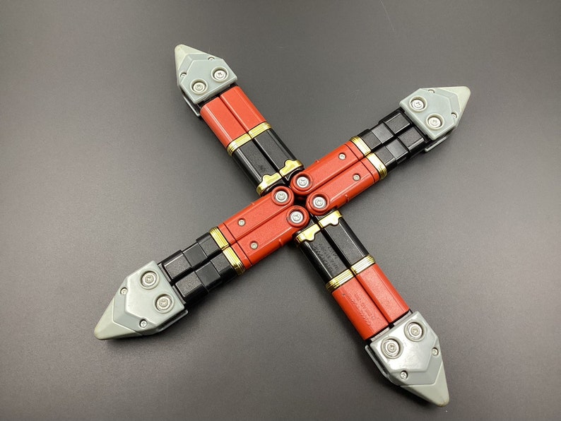 May include: Four red and black toy weapons with gray tips are arranged in a cross shape on a gray surface.