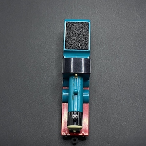 Könnte beinhalten: Ein blauer Spielzeug-Zugmotor mit einem schwarzen Schornstein und roten Rädern. Der Motor hat ein schwarzes Gesicht mit einem weißen Lächeln und schwarzen Augen.