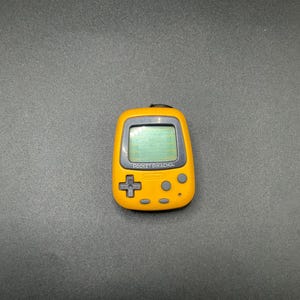 May include: A yellow Pocket Pikachu handheld game console with a gray trim. The device has a small screen, a directional pad, and several buttons. The text "POCKET PIKACHU" is printed on the screen.