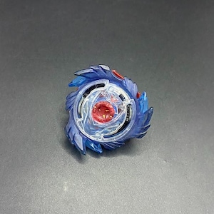 May include: A blue and clear plastic spinning top toy with a red centre. The toy has a multi-layered design with blue blades and a clear central component. The toy is designed for spinning and battling.