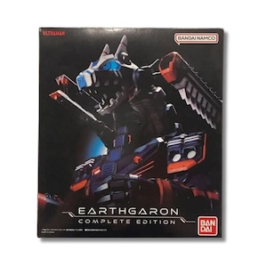 May include: A rectangular product box for the Ultraman Earth Garon Complete Edition by Bandai Namco. The box features a dark background with a graphic illustration of a mechanical creature in blue, black, and orange, with the text Earth Garon.