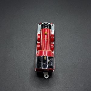 Könnte beinhalten: Eine rote und schwarze Spielzeug-Lokomotive mit silbernen Verzierungen. Die Lokomotive hat einen schwarzen Schornstein und eine goldene Glocke. Die Lokomotive hat eine schwarze Basis mit einem silbernen Schalter.