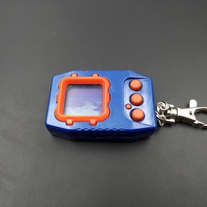 May include: A blue and orange digital pet keychain with a screen and three buttons. The keychain has a silver metal chain and a silver metal clasp.