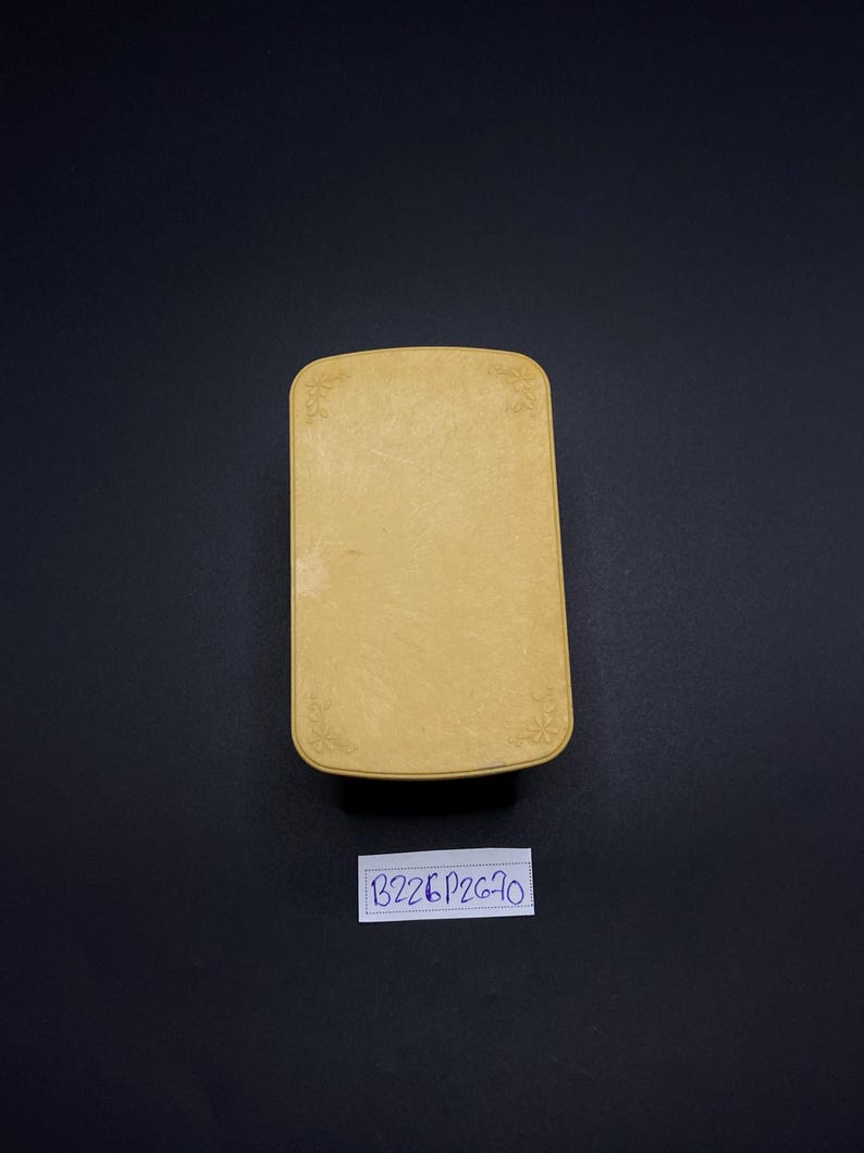 May include: A rectangular, light yellow box with rounded corners and floral corner designs. The box has a textured surface and a label with the text "B226P2670" is below it.