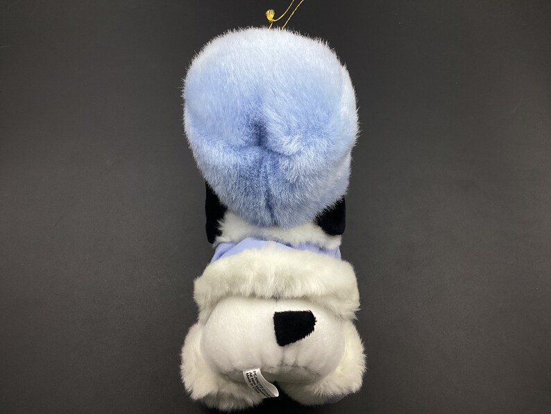 May include: A white plush dog wearing a blue fur hat and a white fur coat. The dog has black eyes and a black nose.