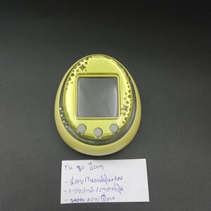 May include: A yellow handheld electronic game with a black screen and three gray buttons. The device has a gold-colored border with star-shaped designs. A handwritten note is below the device.