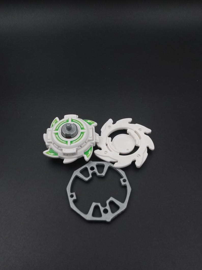 May include: A three-part toy set comprising a white and green top, a white ring, and a silver-coloured ring. The top has a circular design with green accents and text. The other white piece has a star-like design.