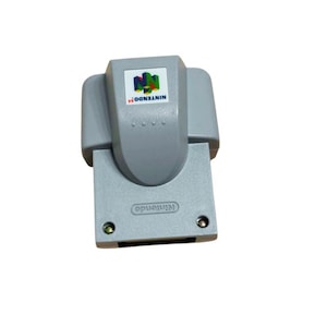 Może przedstawiać: Szary dodatek Nintendo 64 Expansion Pak z prostokątną plastikową obudową i wypukłą częścią środkową. Na górze znajduje się kolorowe logo i napis Nintendo 64, a w dolnej przedniej części wytłoczona jest nazwa marki Nintendo.