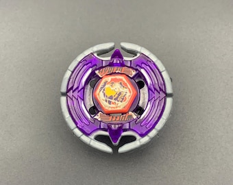 Könnte beinhalten: Ein kreisförmiges, violett-silbernes Kreiselspielzeug mit einem zentralen, orangefarbenen, sechseckigen Bolzen mit grafischem Design. Das Spielzeug hat einen metallisch silbernen Außenring und einen durchscheinenden violetten Kunststoffkörper.