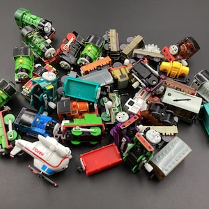 Puede incluir: Una colección de locomotoras y vagones de tren de juguete de colores. Los juguetes están hechos de plástico y presentan varios personajes y diseños.