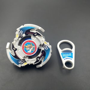 May include: White and blue Beyblade with a red and white circular design featuring a cartoon animal. The Beyblade is accompanied by a white plastic launcher with Japanese text.
