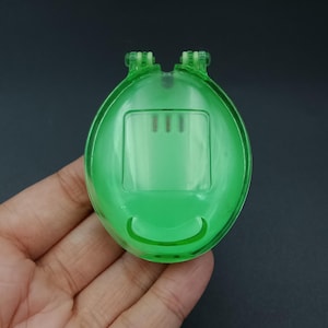 May include: A transparent green plastic oval-shaped object with a rectangular section and three vertical lines. The object has two small protrusions at the top and a curved indentation at the bottom, resembling a smile.