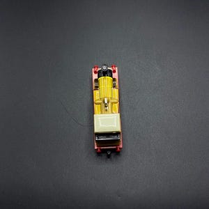 May include: A yellow toy train with a black chimney and a white roof. The train has red wheels and is on a black background.