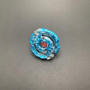 May include: A clear blue and red plastic toy top with a spinning mechanism. The top has a red centre and a clear blue outer ring with a pattern of lines and circles.