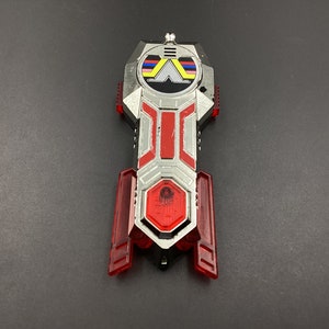 May include: A silver and red toy with a black and white logo featuring a stylised letter A. The toy has a red light in the centre.