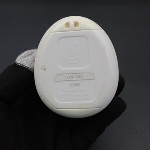 Puede incluir: Un dispositivo electr&oacute;nico blanco de forma ovalada con un panel rectangular y dos peque&ntilde;as protuberancias en la parte superior. El dispositivo tiene los n&uacute;meros "2250336" y "81804" impresos. El dispositivo es sostenido por una mano enguantada.