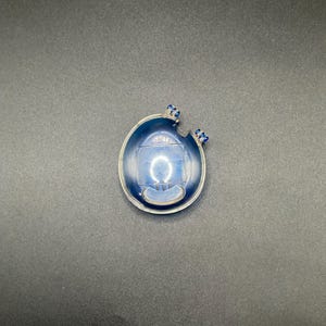 May include: A blue and clear glass pendant with a circular design. The pendant has a rounded shape with a deep blue interior and small blue accents. The pendant is likely a piece of jewellery.