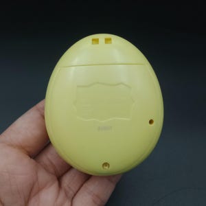 May include: A pale yellow, egg-shaped handheld electronic device. The device has two small square openings at the top and two small circular openings at the bottom. The back of the device has text and the number "42801".