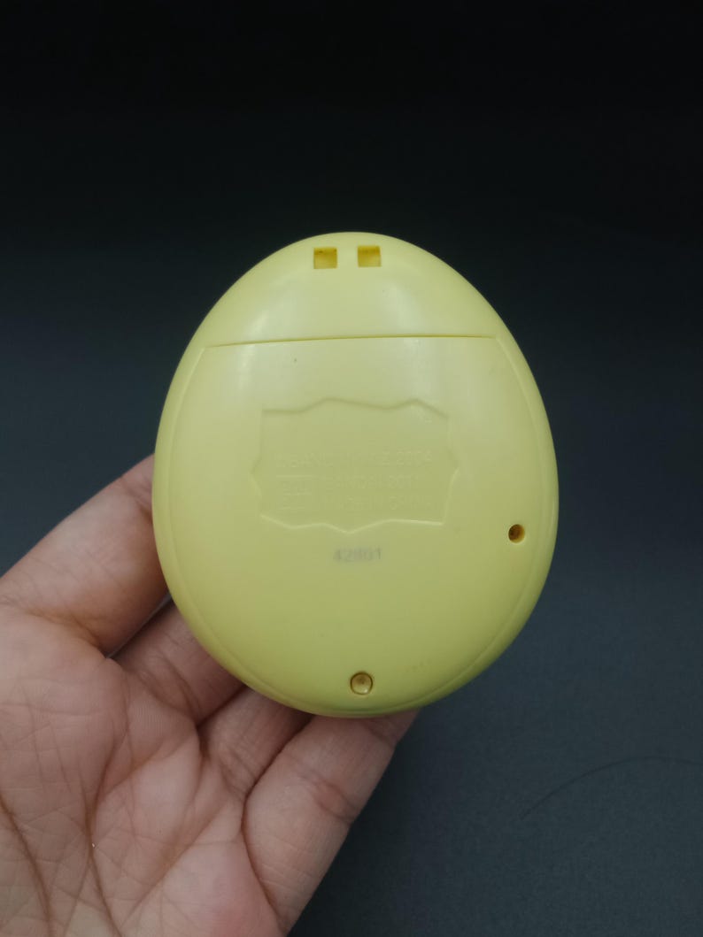 May include: A pale yellow, egg-shaped handheld electronic device. The device has two small square openings at the top and two small circular openings at the bottom. The back of the device has text and the number "42801".